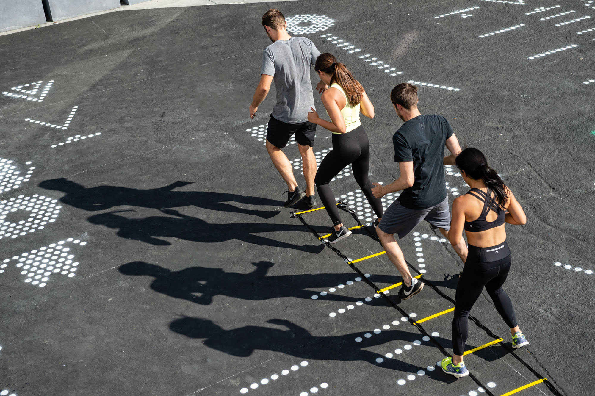 Four people exercising on an agility ladder at an outdoor Public Recreation site